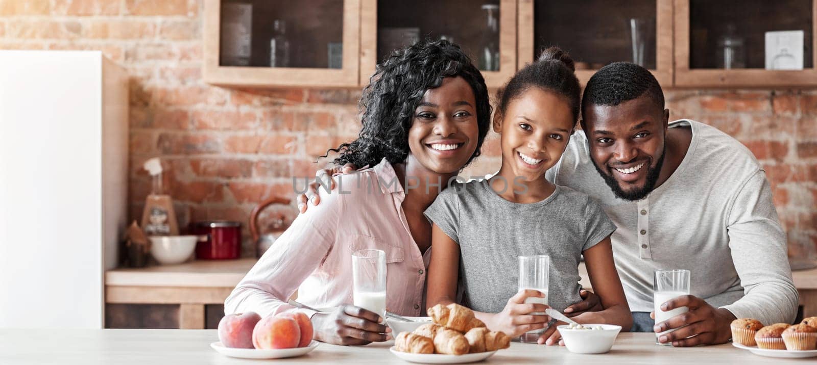 Beautiful black family having breakfast together, drinking milk and eating sweets at kitchen, copy space