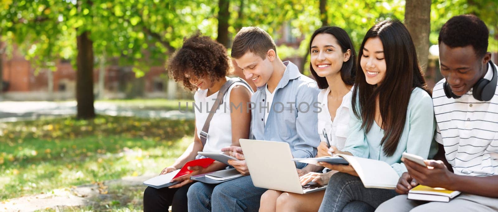 Group of international students preparing for classes together in university courtyard, smiling and enjoying summer weather