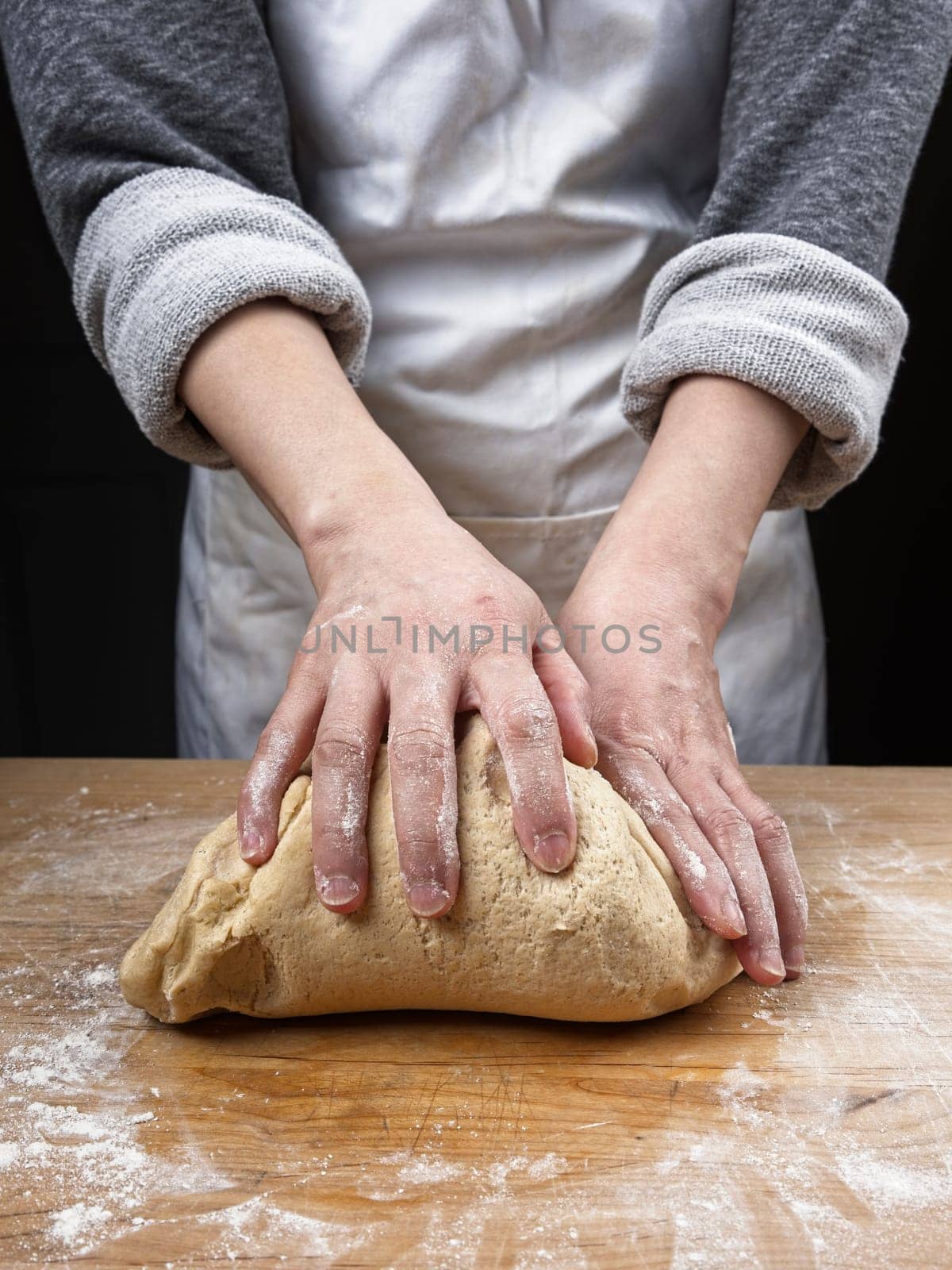 A close up photo of a woman's hands kneading a big ball of dough on a wooden cutting board.