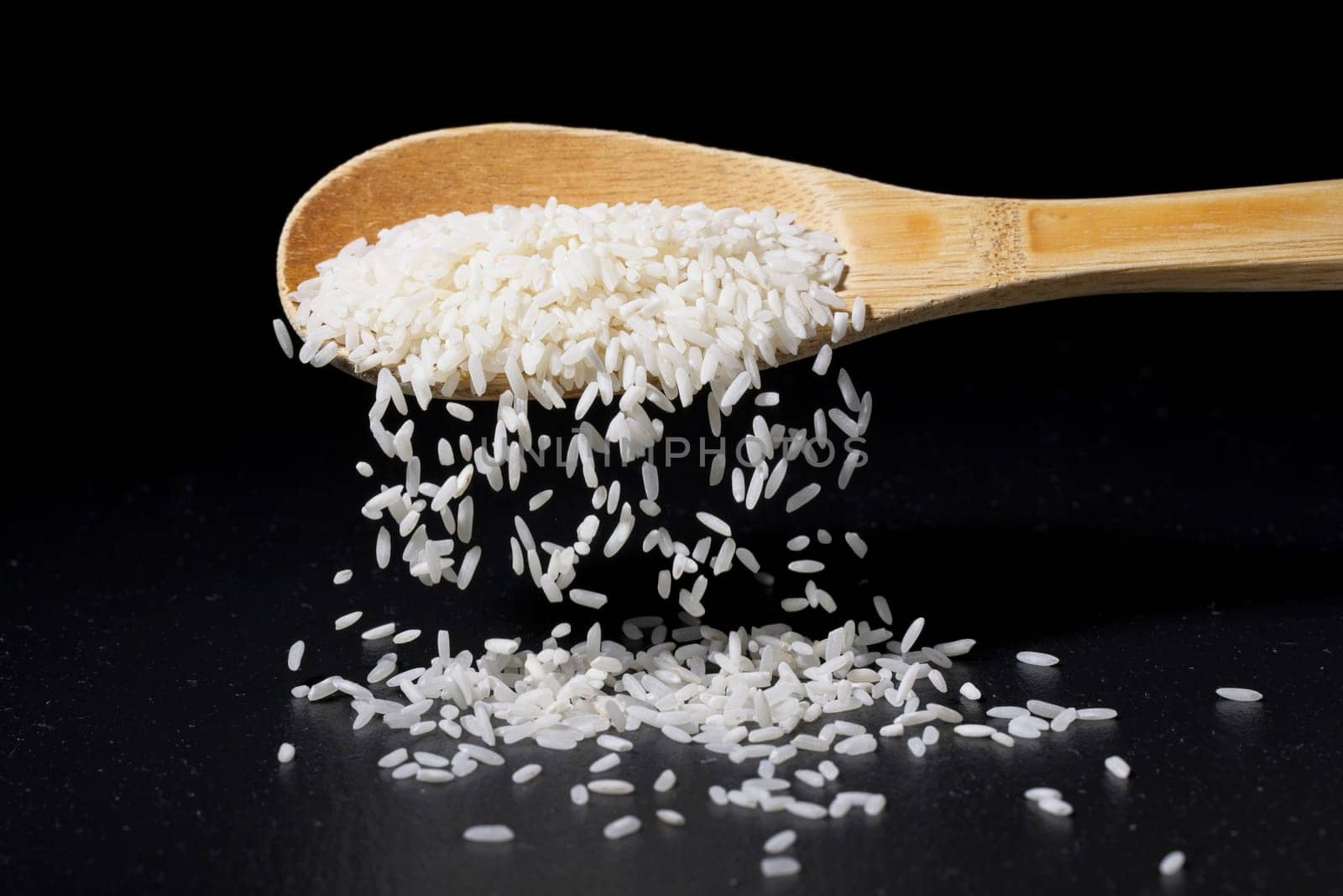 A conceptual photo of long grain white rice pouring off a wooden spoon and spilling onto the floor.