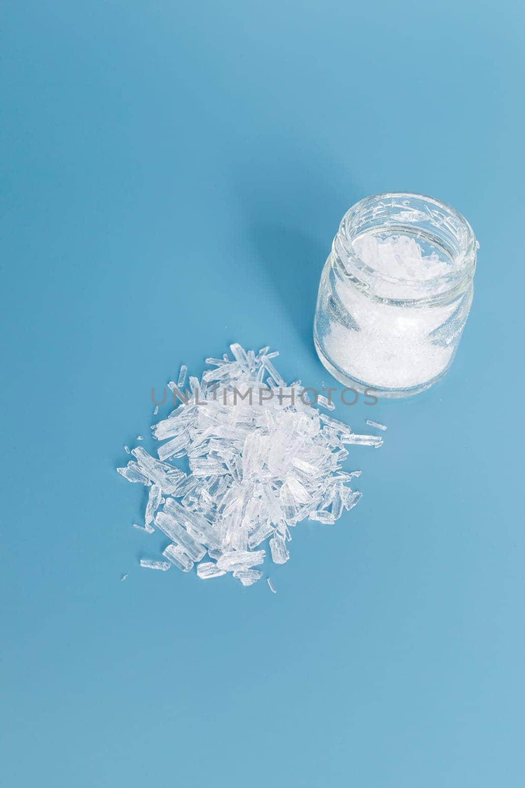 Top View Heap of Translucent Menthol Crystals on Blue Background, Glass Jar. Natural Ingredient for Producing Cosmetics. Vertical Copy Space. High quality photo