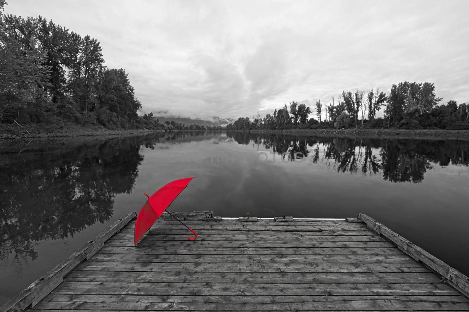 A concept black and white photo of a red umbrella resting on a wooden dock by Kootenai RIver in north Idaho.