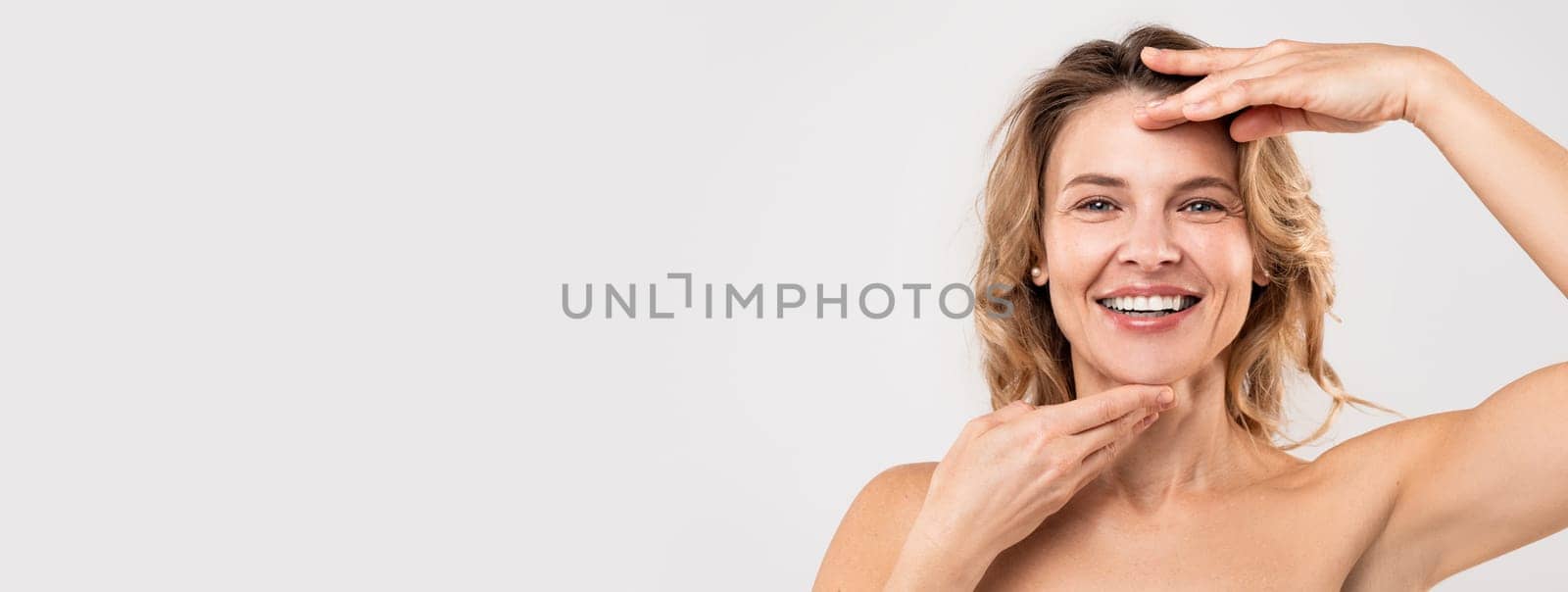 Facebuilding Concept. Happy Beautiful Middle Aged Woman Touching Chin And Forehead And Smiling At Camera, Attractive Mature Lady Massaging Face, Enjoying Anti-Aging Beauty Treatments, Copy Space