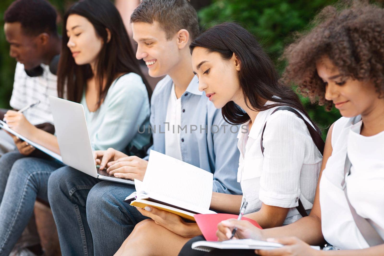 Multicultural group of students studying together outdoors, preparing for classes at campus