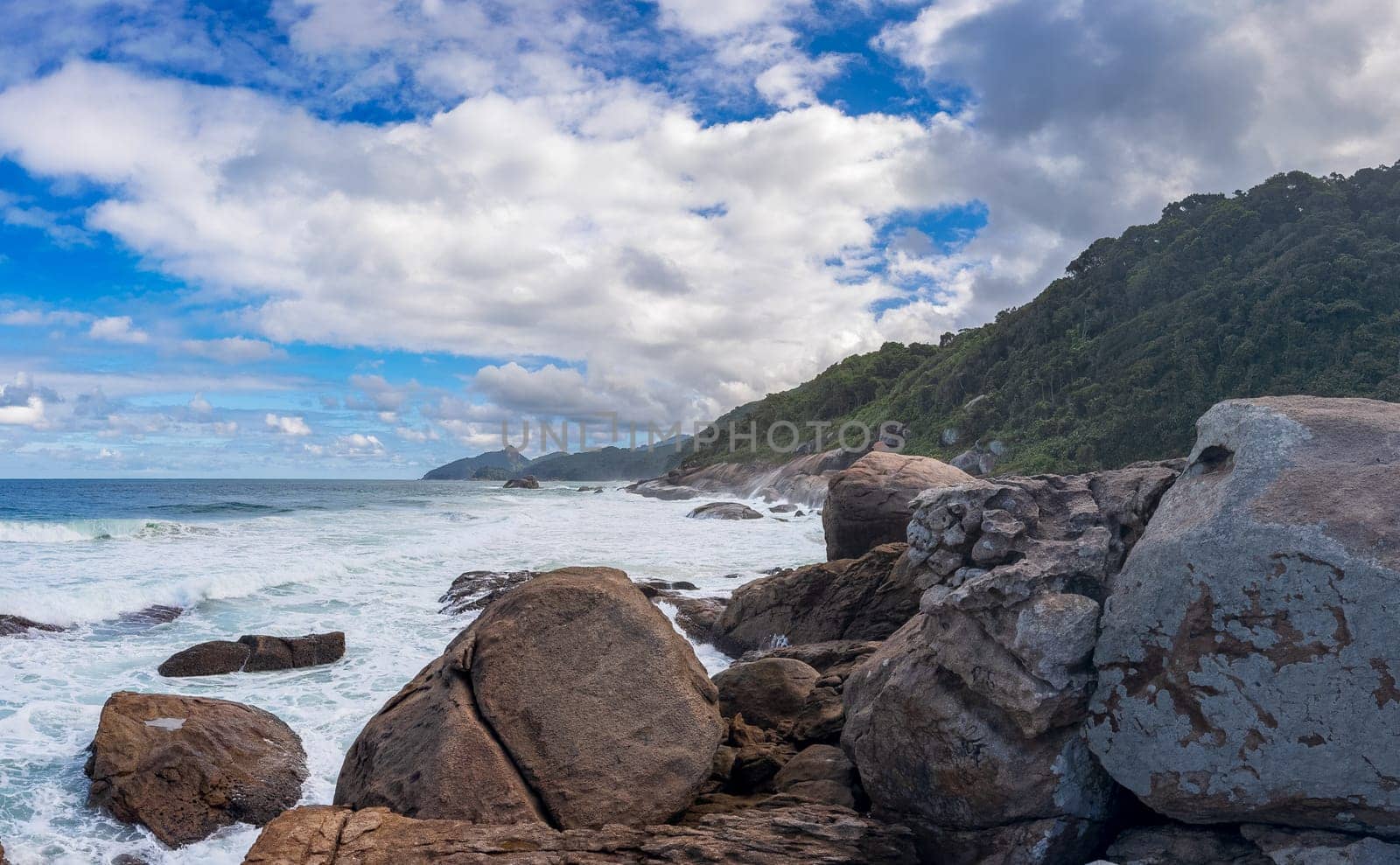 A tranquil coastal view with waves breaking on textured rocks beneath a clear blue sky.