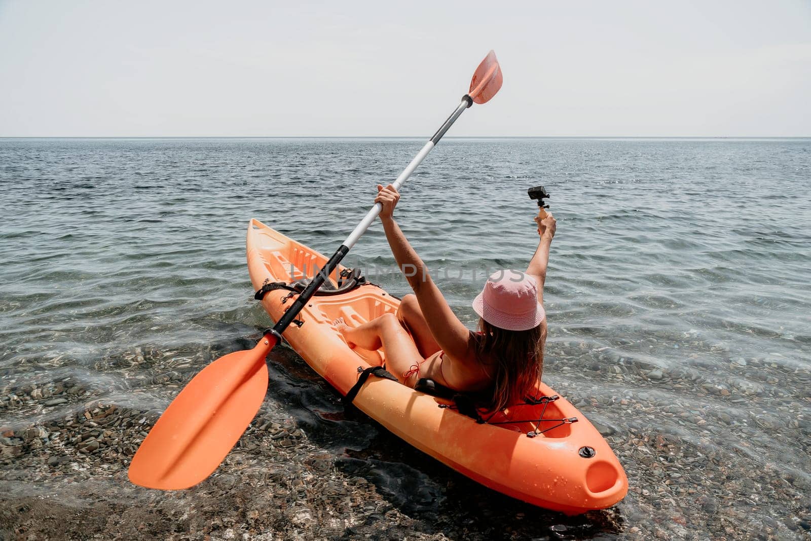 Happy smiling woman in kayak on ocean, paddling with wooden oar. Calm sea water and horizon in background