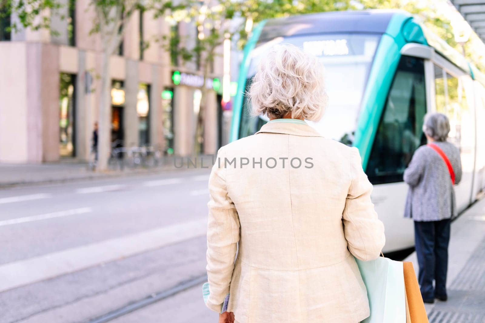 unrecognizable mature woman standing with shopping bags waiting for public transport, concept of sustainable mobility and urban lifestyle, copyspace for text