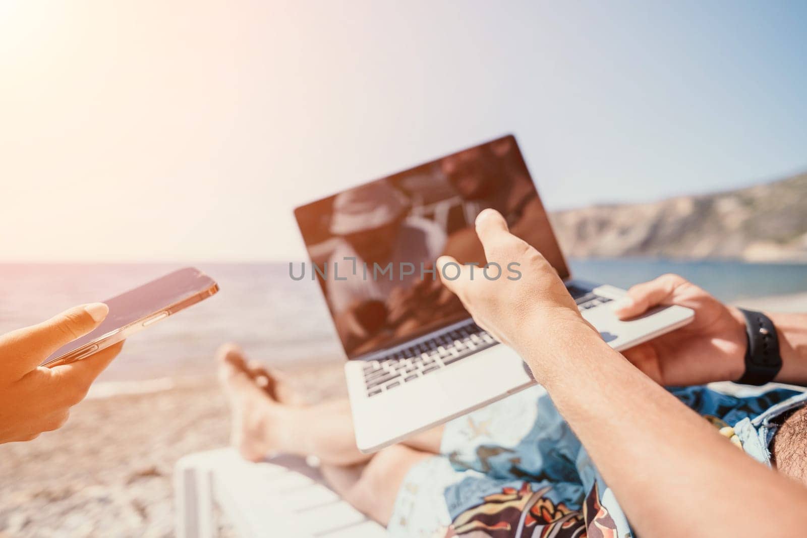 Digital nomad, Business man working on laptop by the sea. Man typing on computer by the sea at sunset, makes a business transaction online from a distance. Freelance, remote work on vacation
