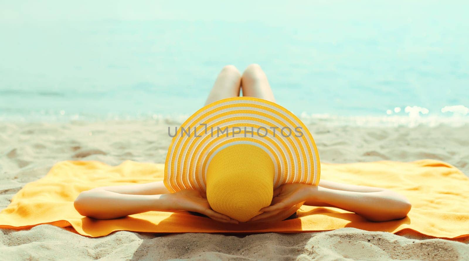 Summer vacation, beautiful happy relaxing young woman with yellow straw tourist hat lying on sand on the beach at sea