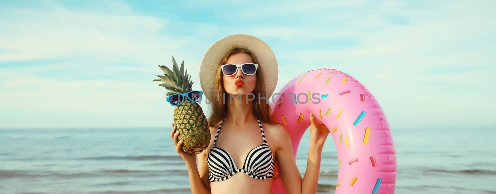 Summer vacation, tourism, happy young woman with swimming inflatable ring, pineapple fruits, tourist hat and glasses on the beach against sea background