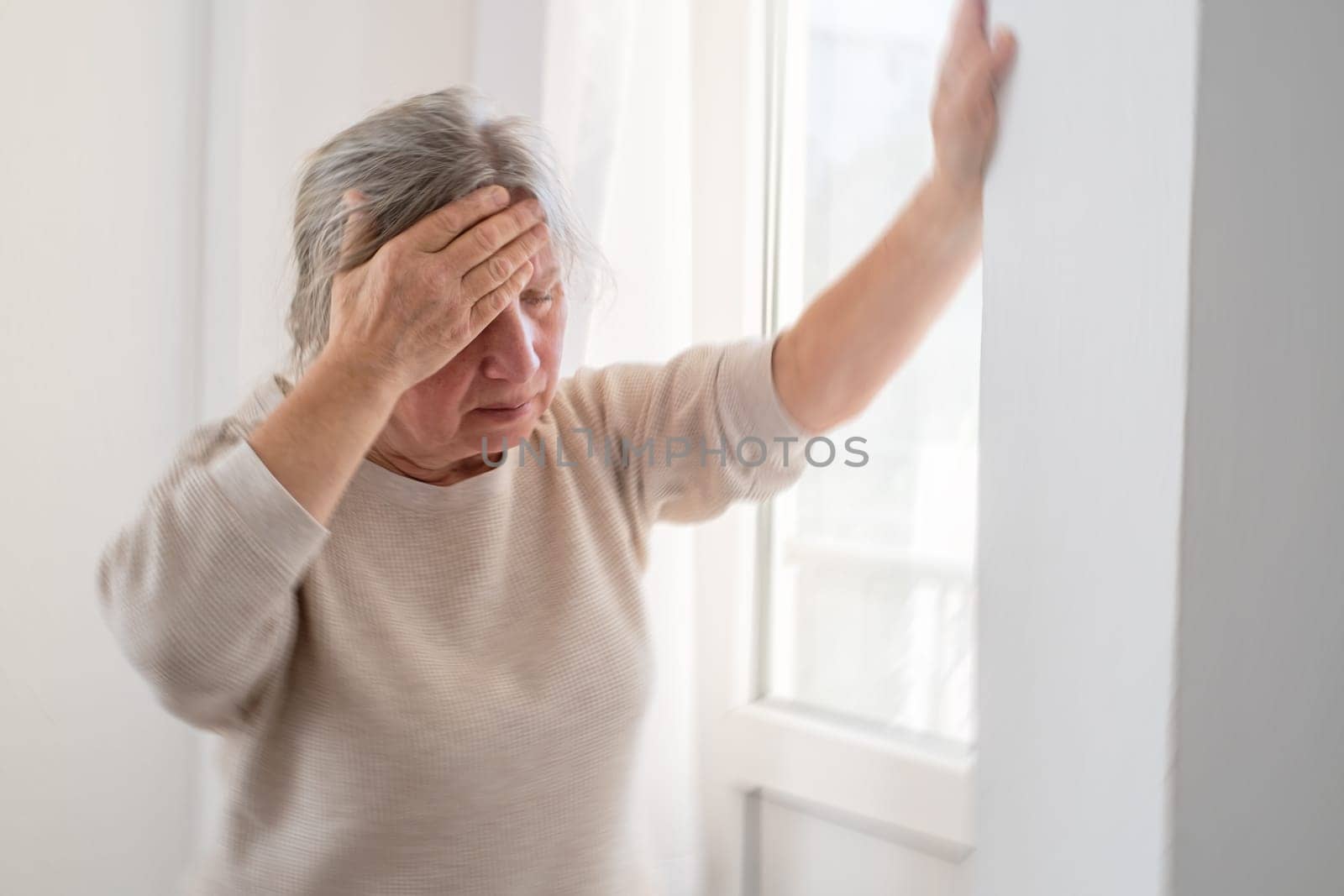 Unhappy mature woman touching head, feeling strong headache, at home alone, upset older female suffering from migraine or high blood pressure