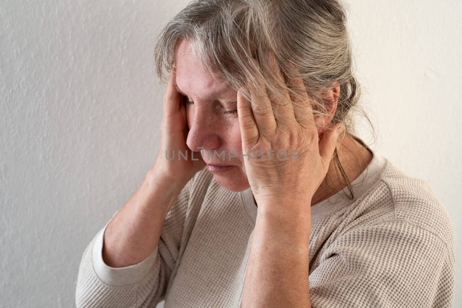 Unhappy mature woman touching head, feeling strong headache, at home alone, upset older female suffering from migraine or high blood pressure