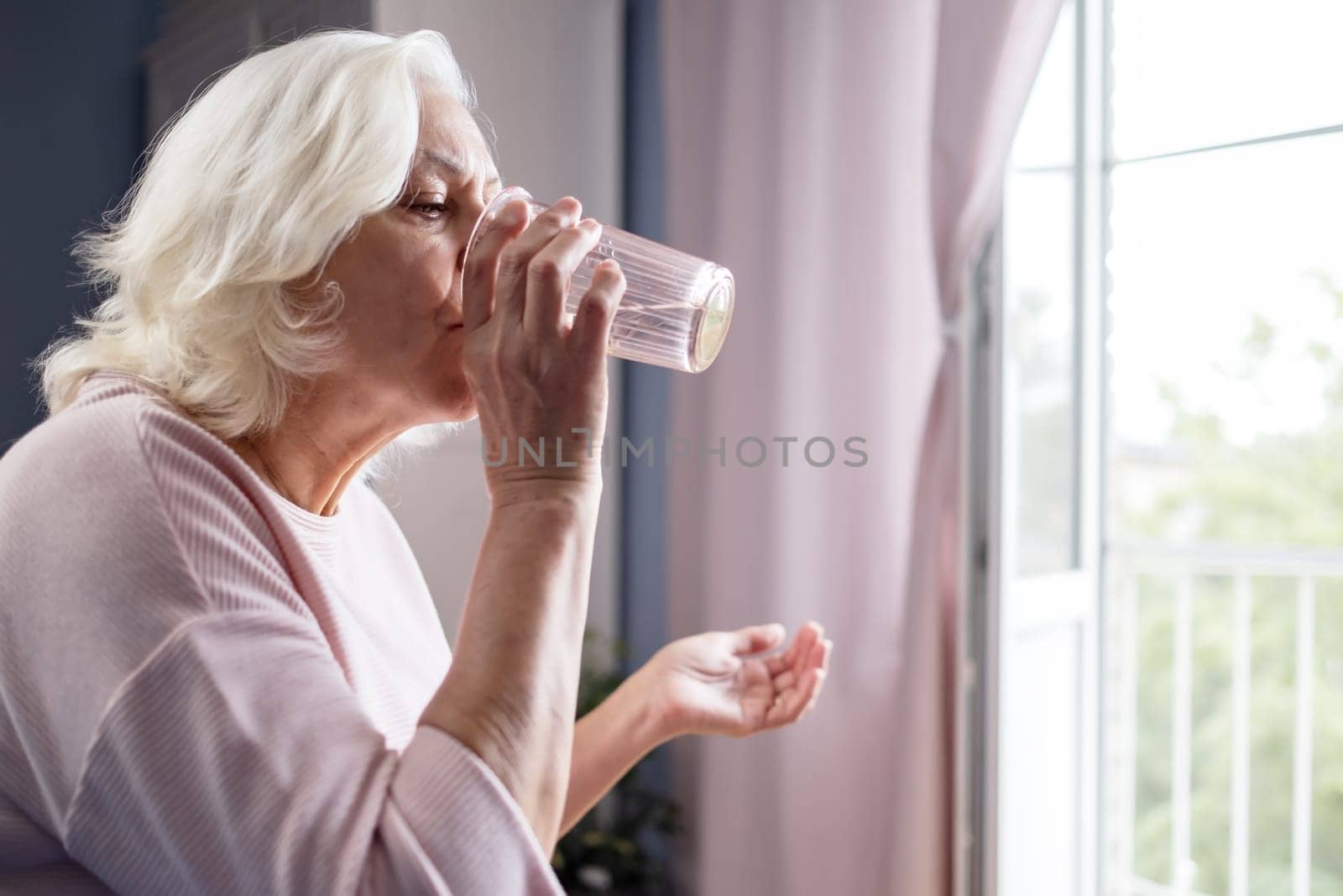 Senior woman takes pill with glass of water in hand. Stressed female drinking sedated antidepressant meds. Woman feels depressed, taking drugs.