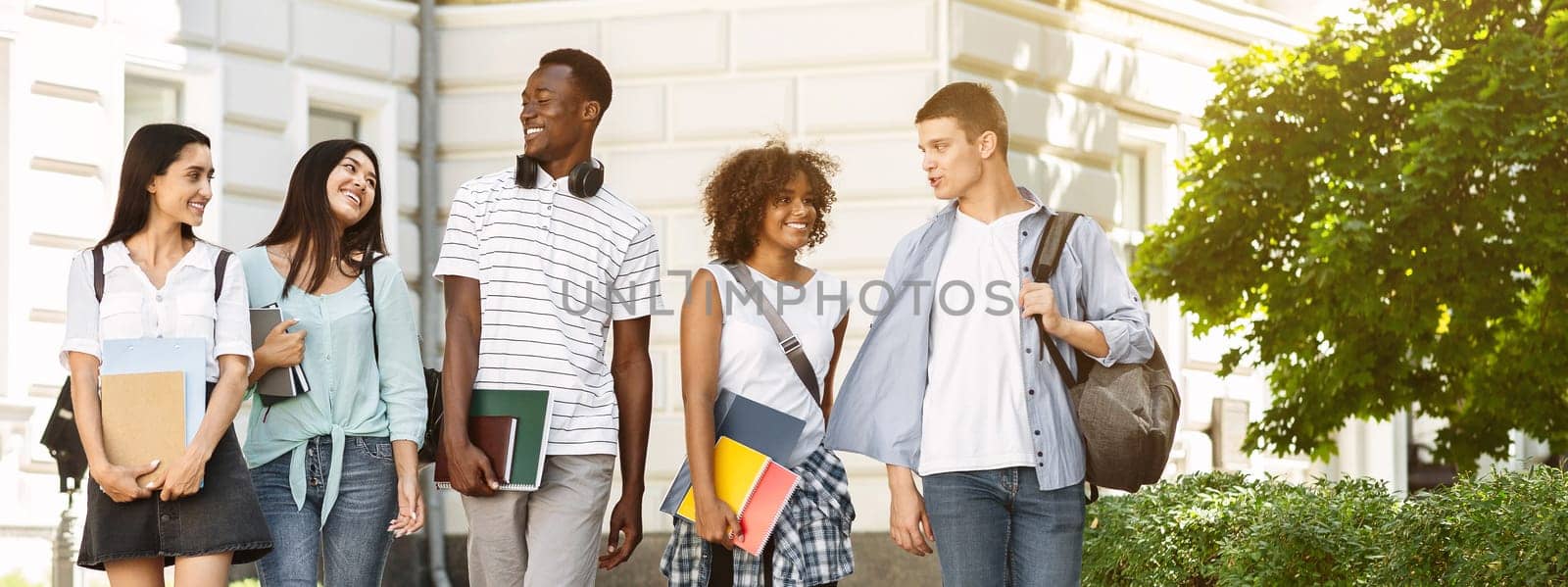 Campus Life. Group of international students walking outdoors after classes, holding workbooks, chatting together and smiling