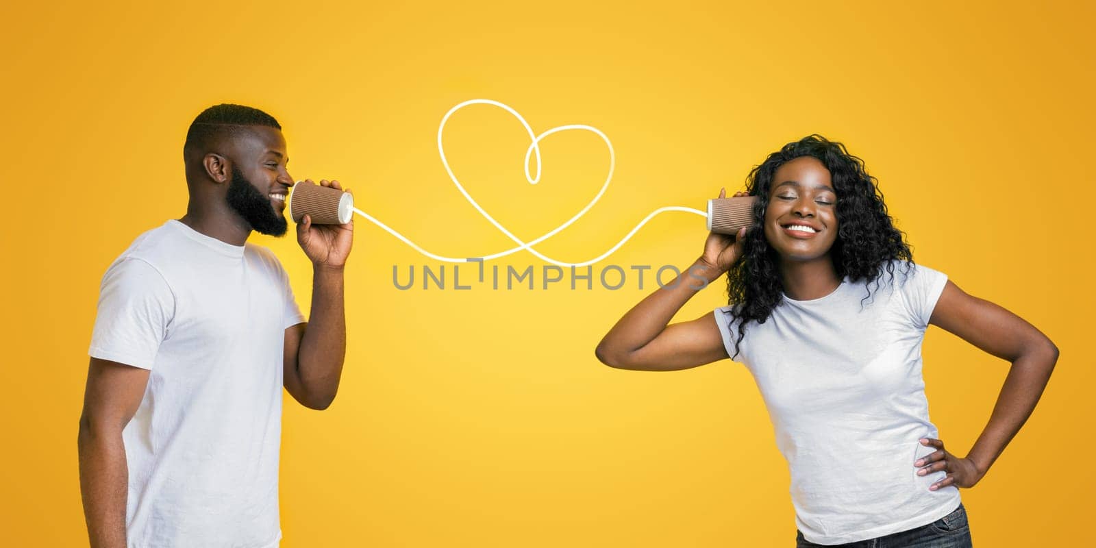 Communication and fun. Young black couple talking through tin can phone, yellow background