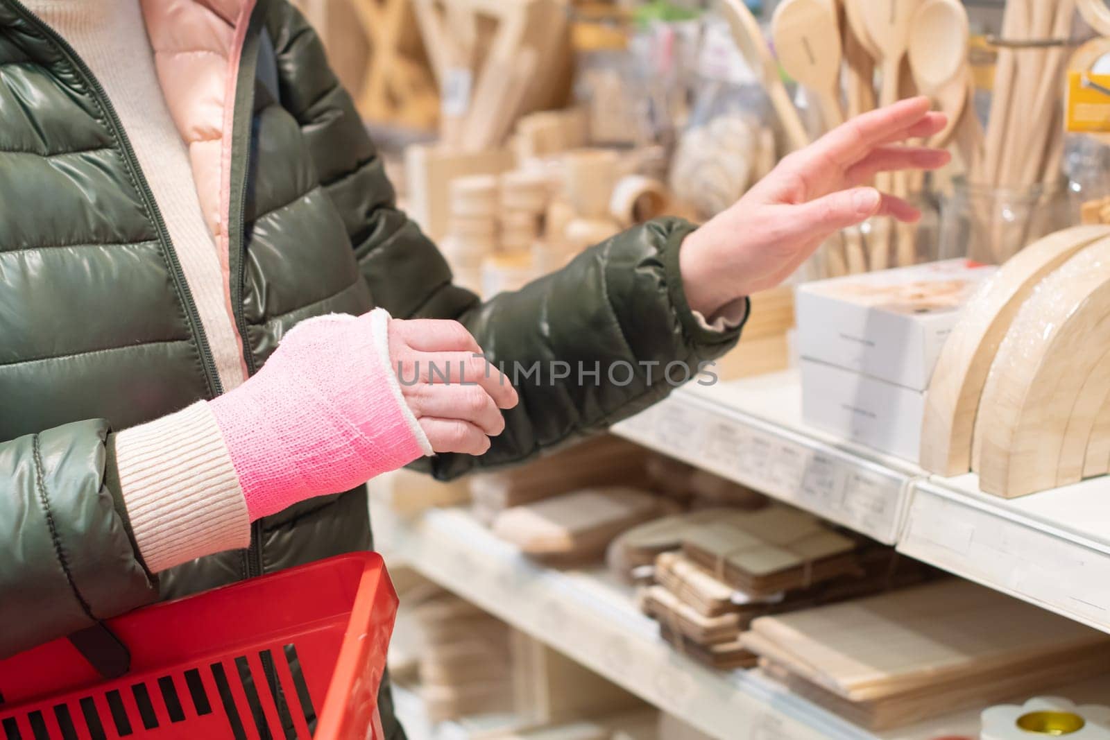 woman with pink cast on her right arm walks through a store with a red shopping basket, leading an active lifestyle despite restrictions