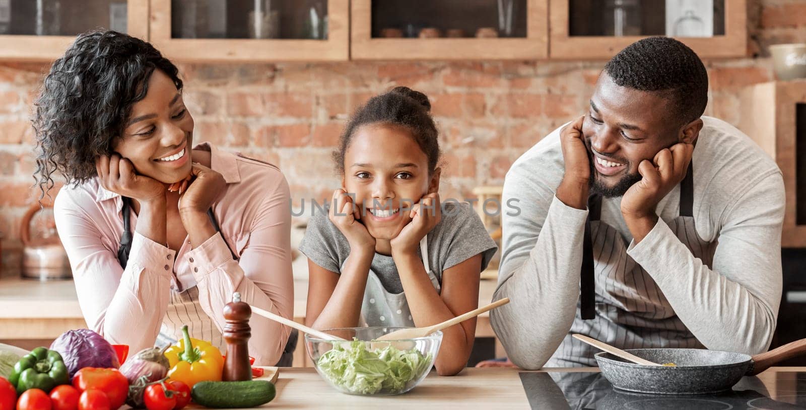 Happy afro family cooking healthy dinner together at kitchen, posing at camera, making salad, panorama with copy space