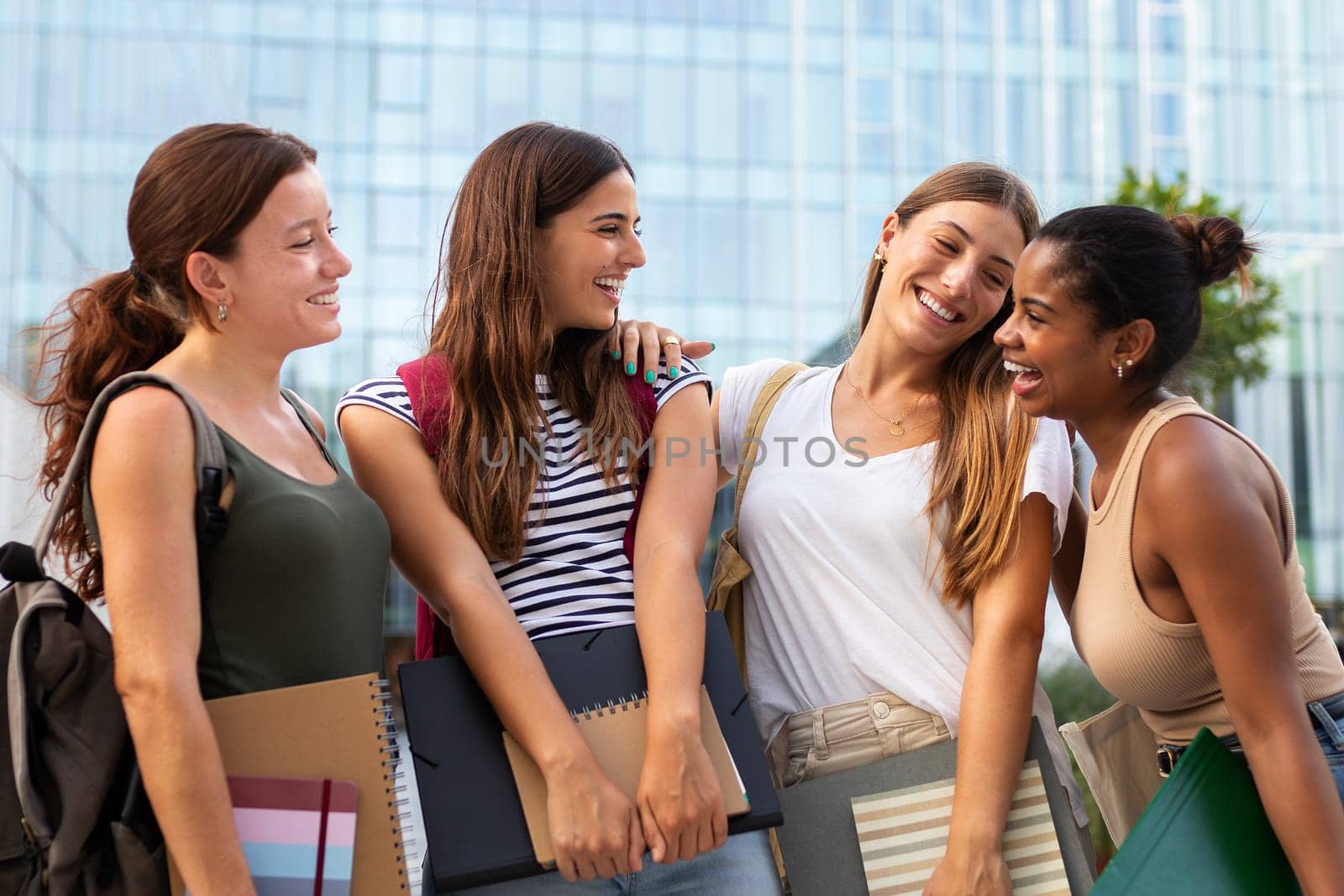 Group of happy multiethnic female college students friends standing outside in campus laughing and having fun. by Hoverstock