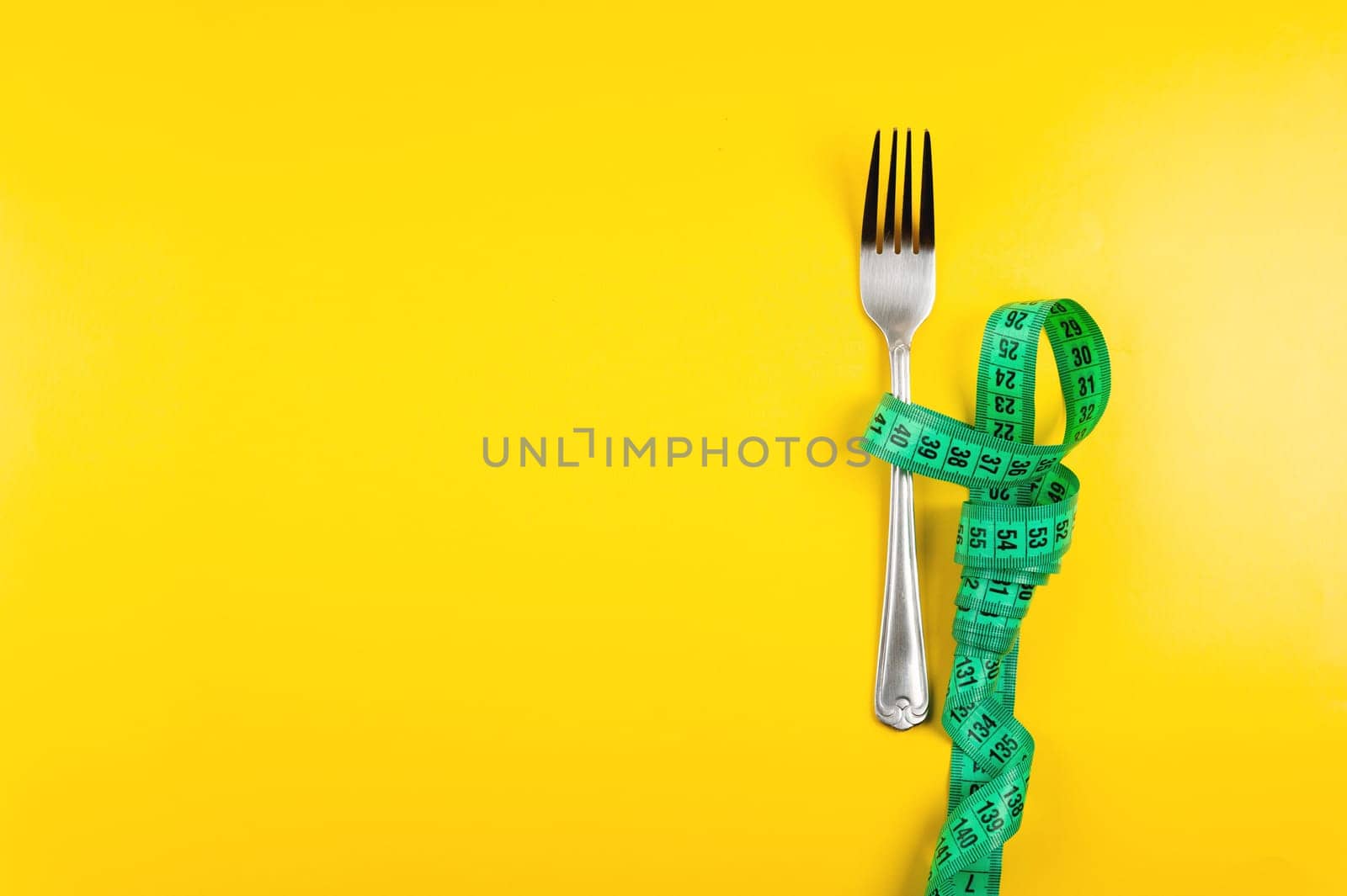 bright green measuring tape with a fork lies on a yellow background, top view. Healthy food idea go diet for banner by yanik88