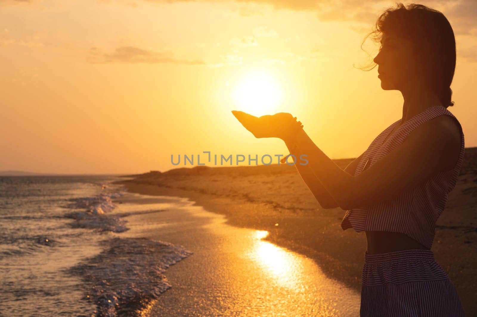 The sun on a woman's hand. Portrait of a young woman in the form of a silhouette and hands holding the sun on the seashore.