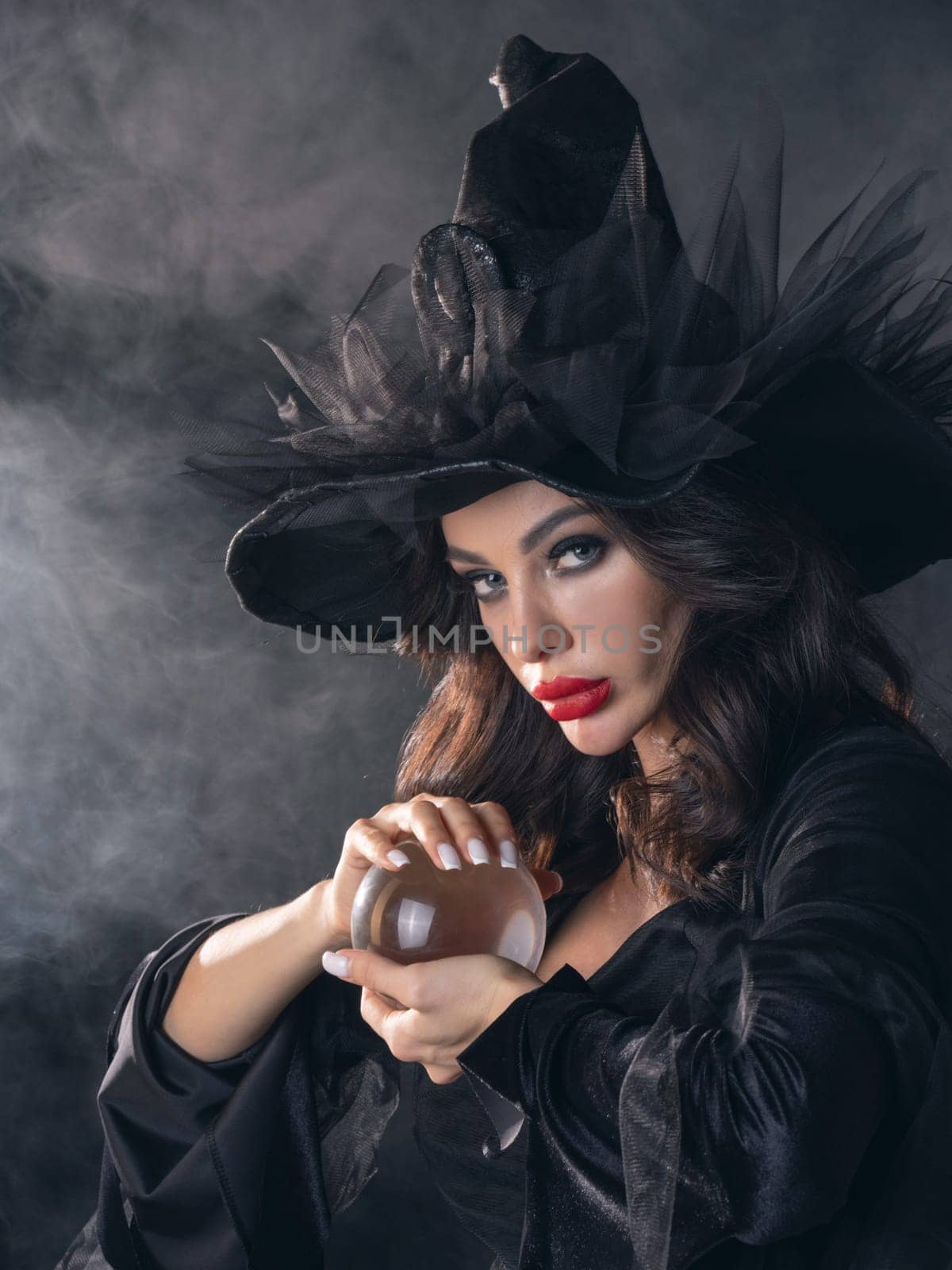 Woman in Halloween witch fortune teller costume with crystal ball. Beautiful sexy model girl in sinister costume and make up