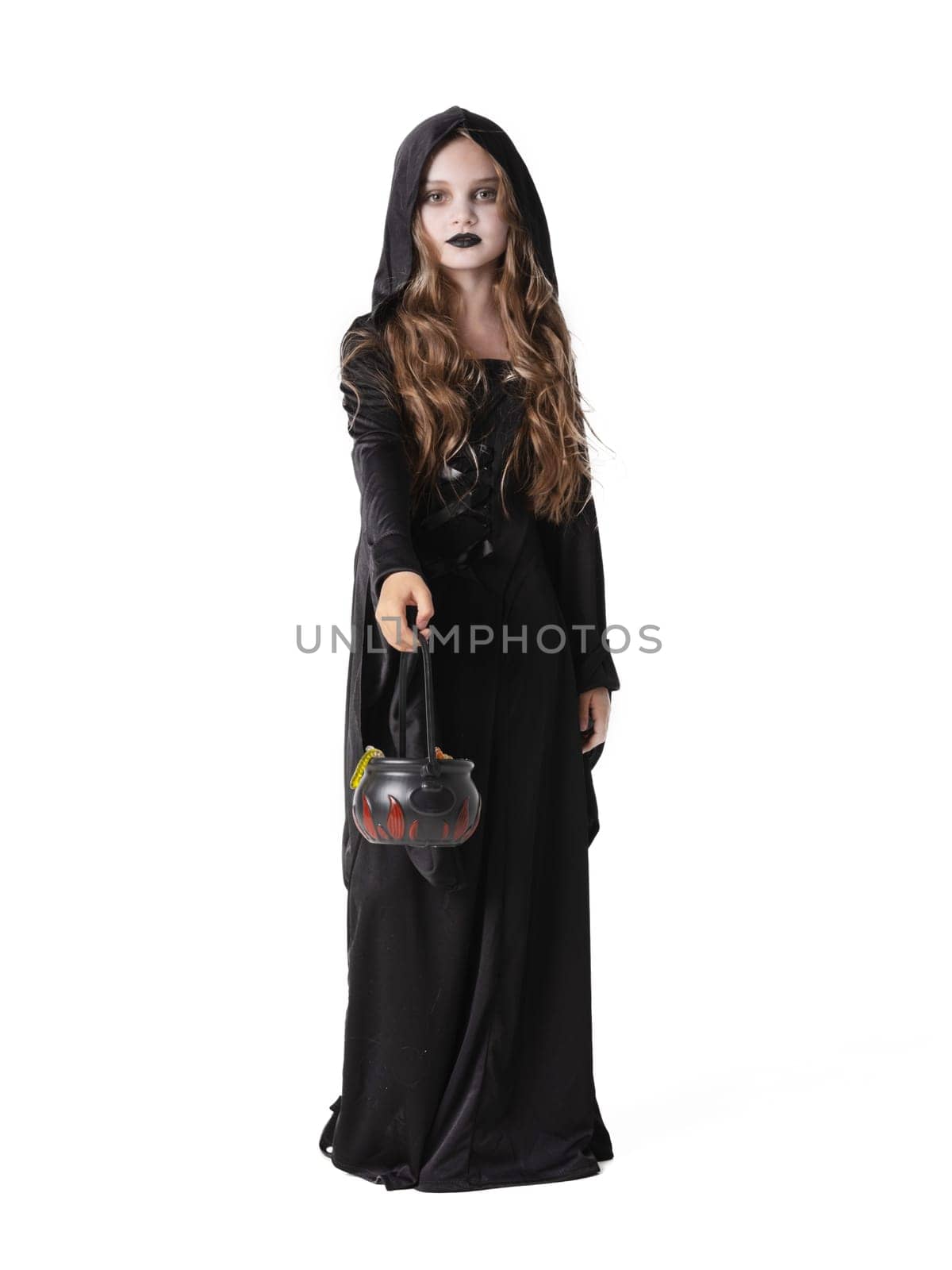 Portrait of little girl in black cloak clothing with cauldron basket of worm sweets isolated on white background, Halloween witch costume, party time, going trick or treating.