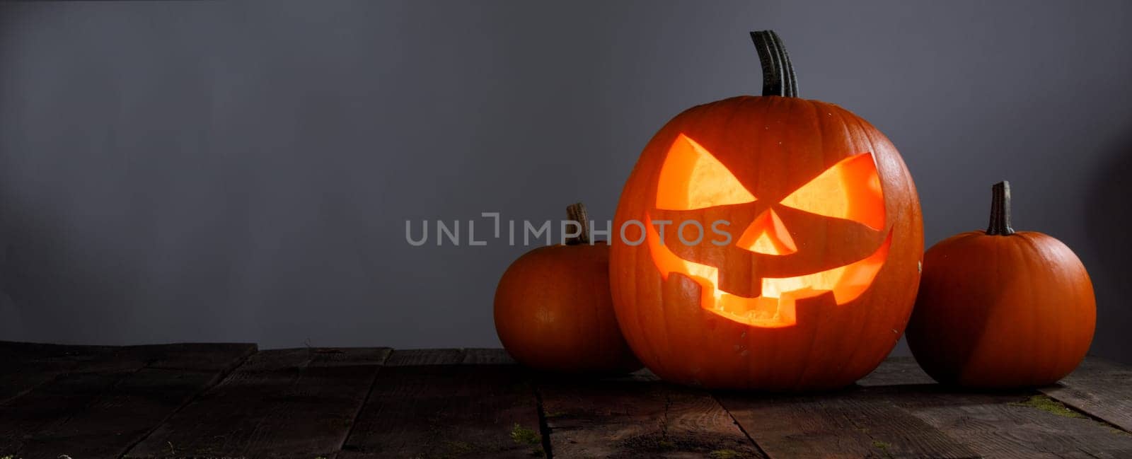 Glowing Halloween pumpkin head jack lantern on wooden table over gray background with copy space for text