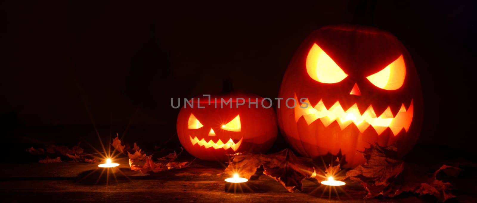 Three glowing Halloween Pumpkin lanterns and burning candles on dark wooden background