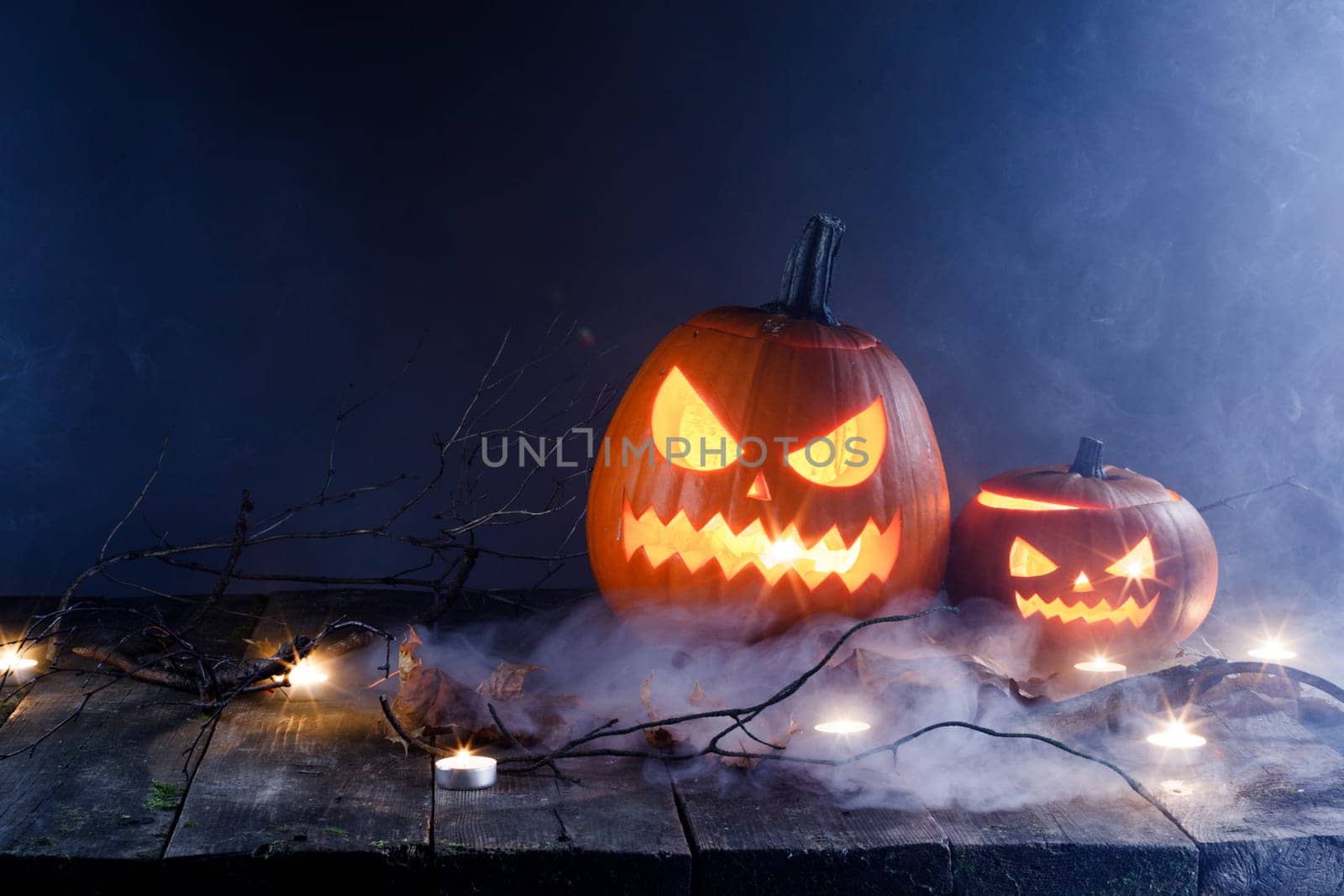 Halloween pumpkins head jack o lantern, candles and dry maple leaves in mist