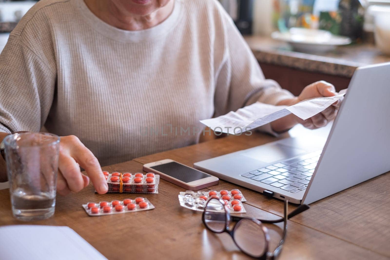 Hand of senior woman holding leaflet to prescribed medicine, pills lying beside on table. Closeup patient reading information sheet.