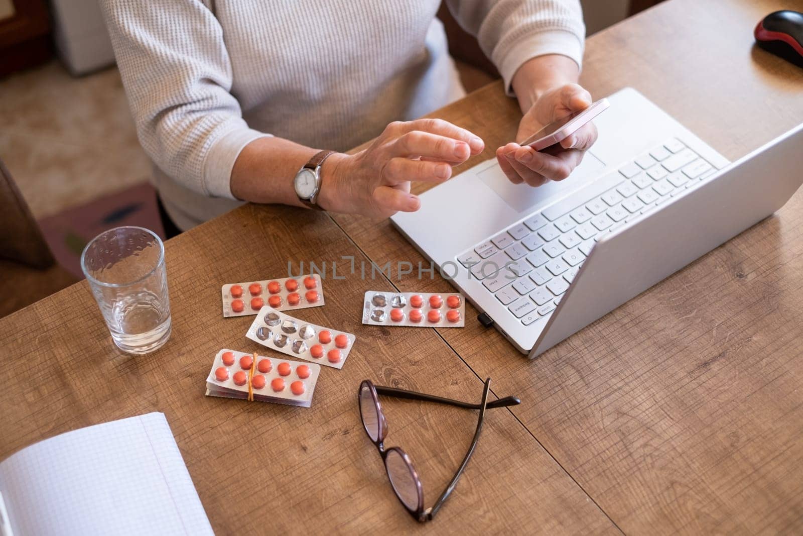 Hand of senior woman holding leaflet to prescribed medicine, pills lying beside on table. Closeup patient reading information sheet.