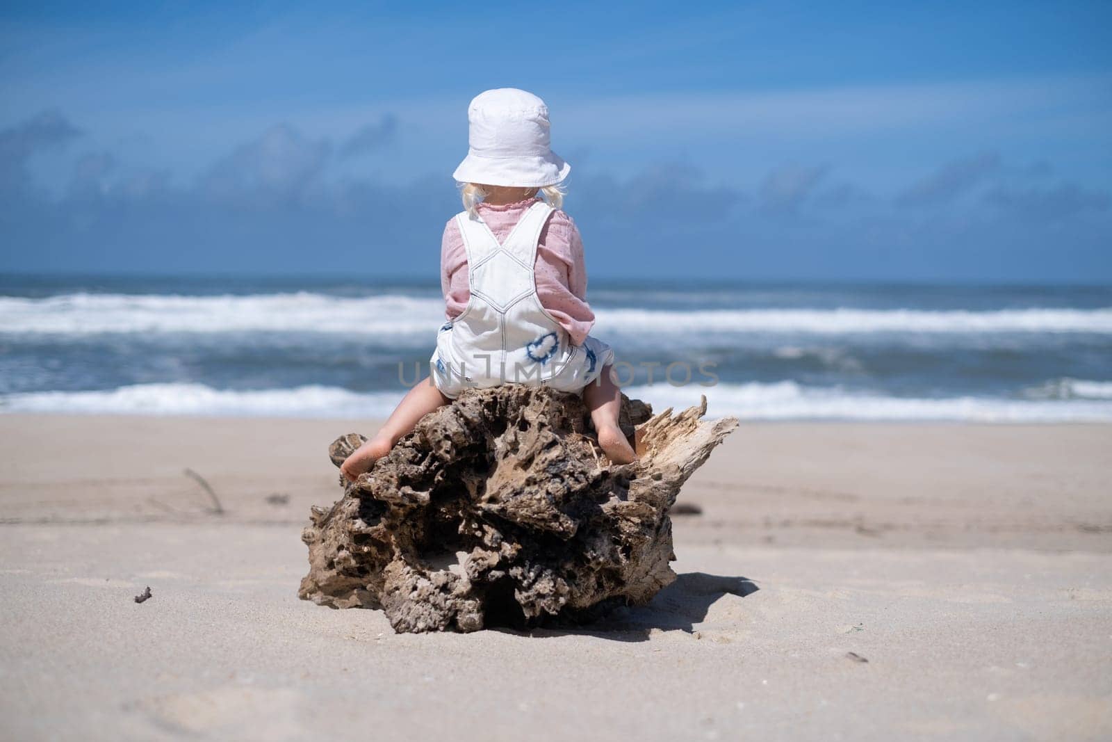 Little girl on sand and playing at sea beach in warm sunny summer day