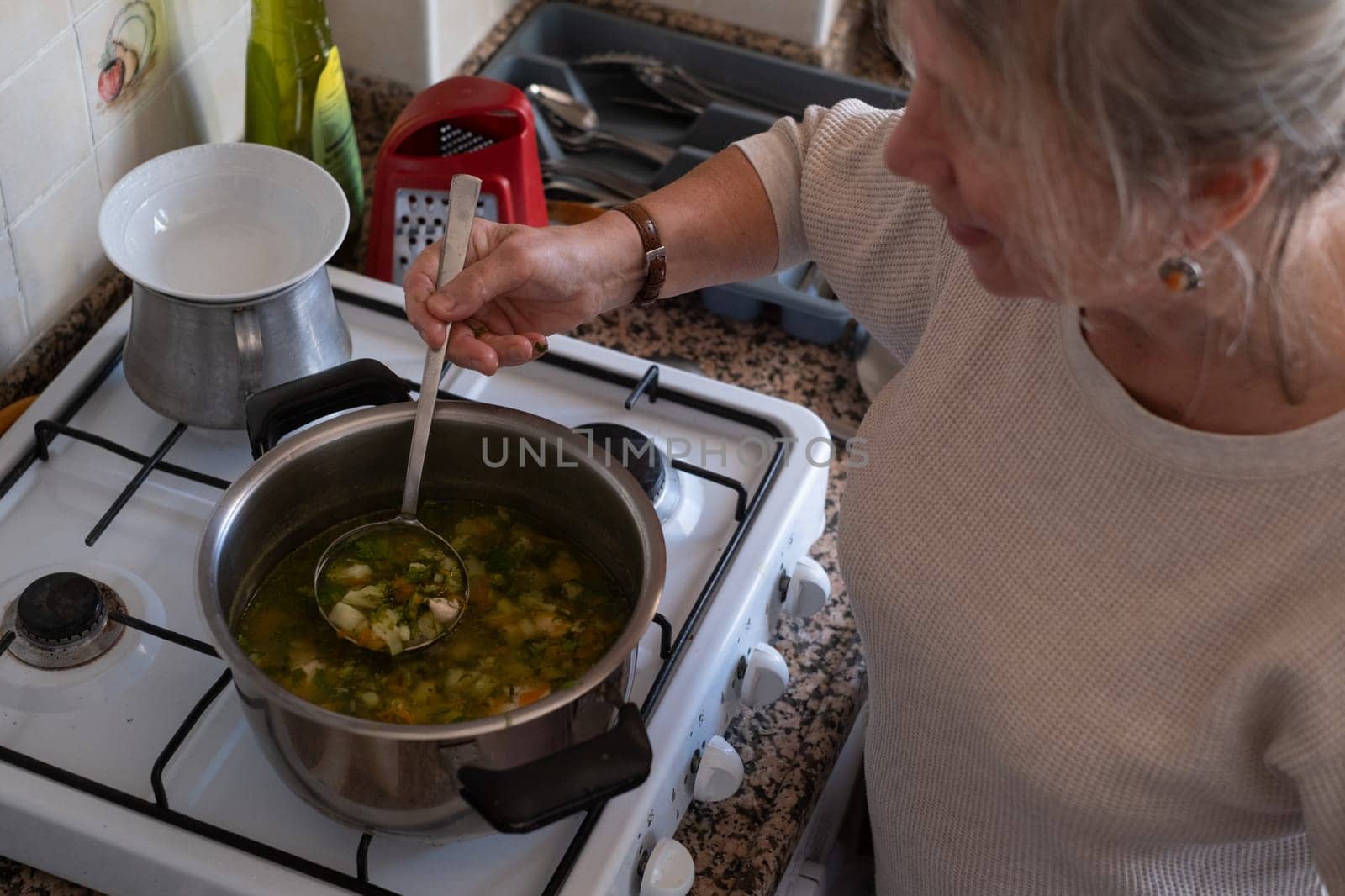 Senior old eldery aged woman grandmother cooking soup in kitchen at home. Grandma preparing food, meal. Healthy food, vegetarian concept. Dieting and healthy lifestyle.