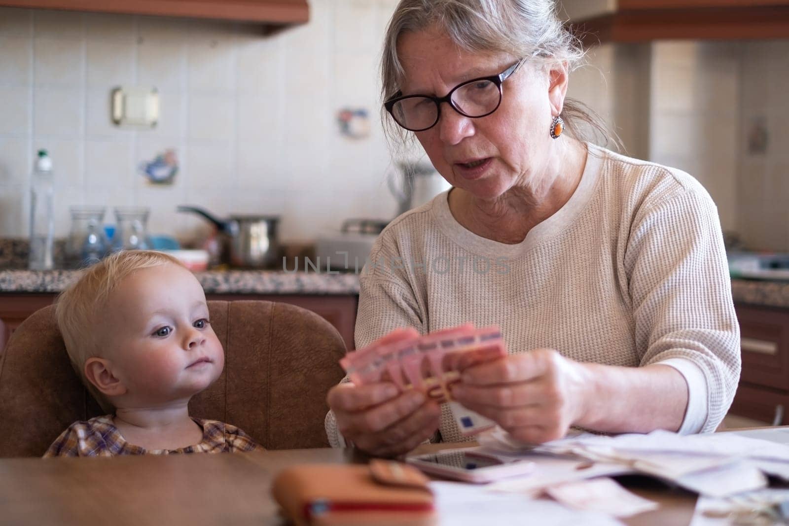 Senior woman counting money americain dollars and euro at home teaching kid financial literacy planning budget together with little child.