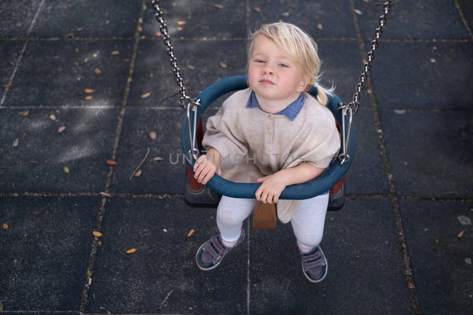 Cute smiling kid girl playing on a swing outdoor on a playground. Children summer activity.