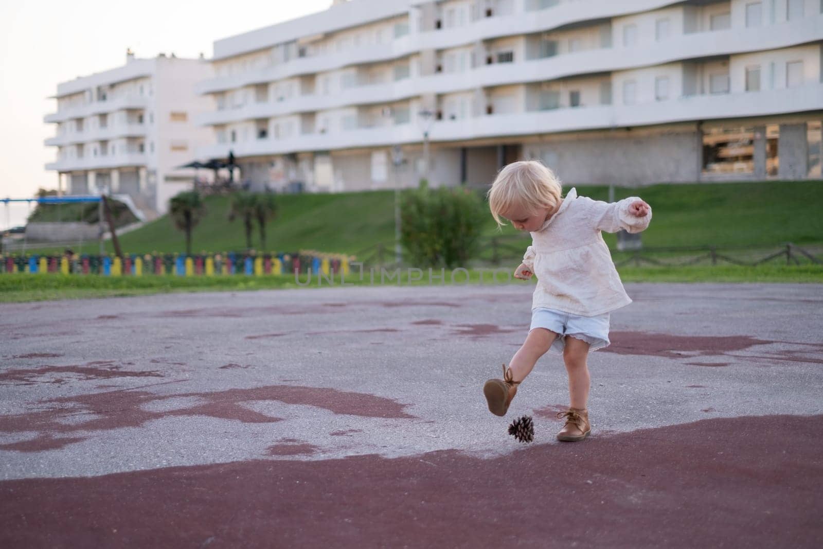 Little girl playing with a cone as it is a ball. Toys from nature