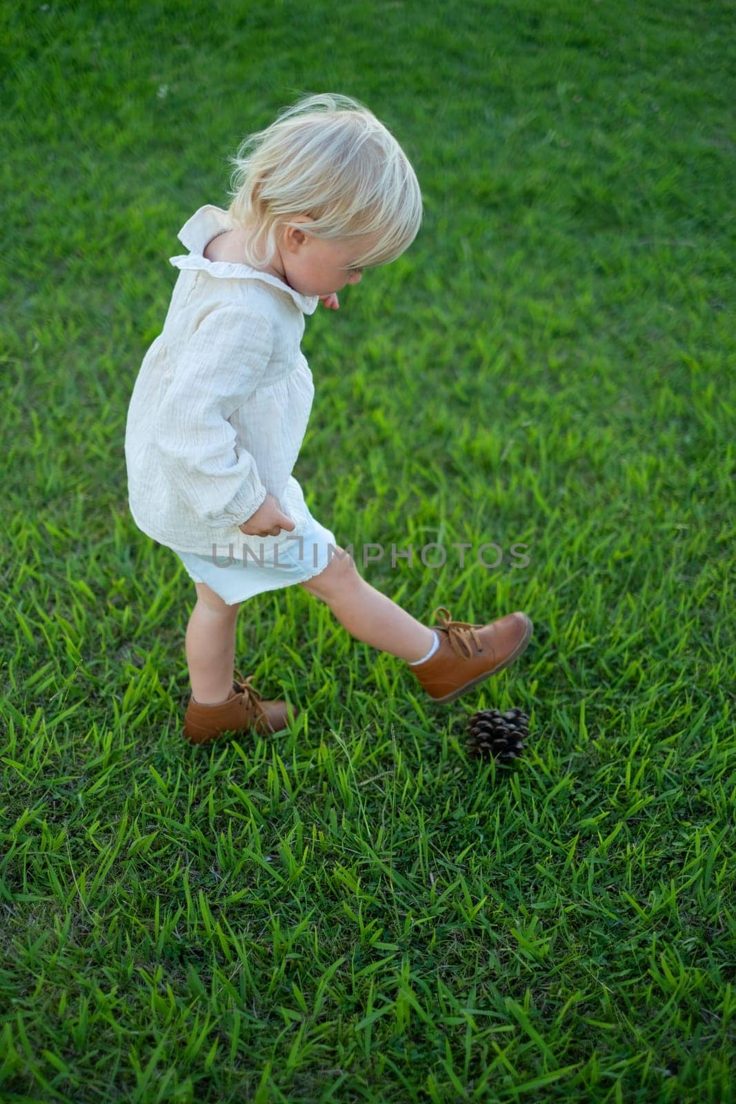 Little girl playing with a cone as it is a ball. Toys from nature