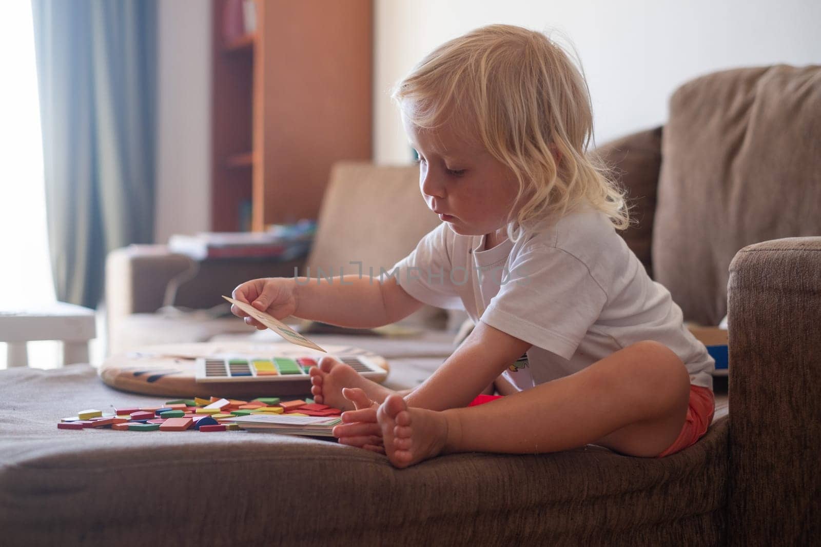 Little toddler plays on the bed in a wooden constructor, preschool child learning at home to make mosaic. Early development.