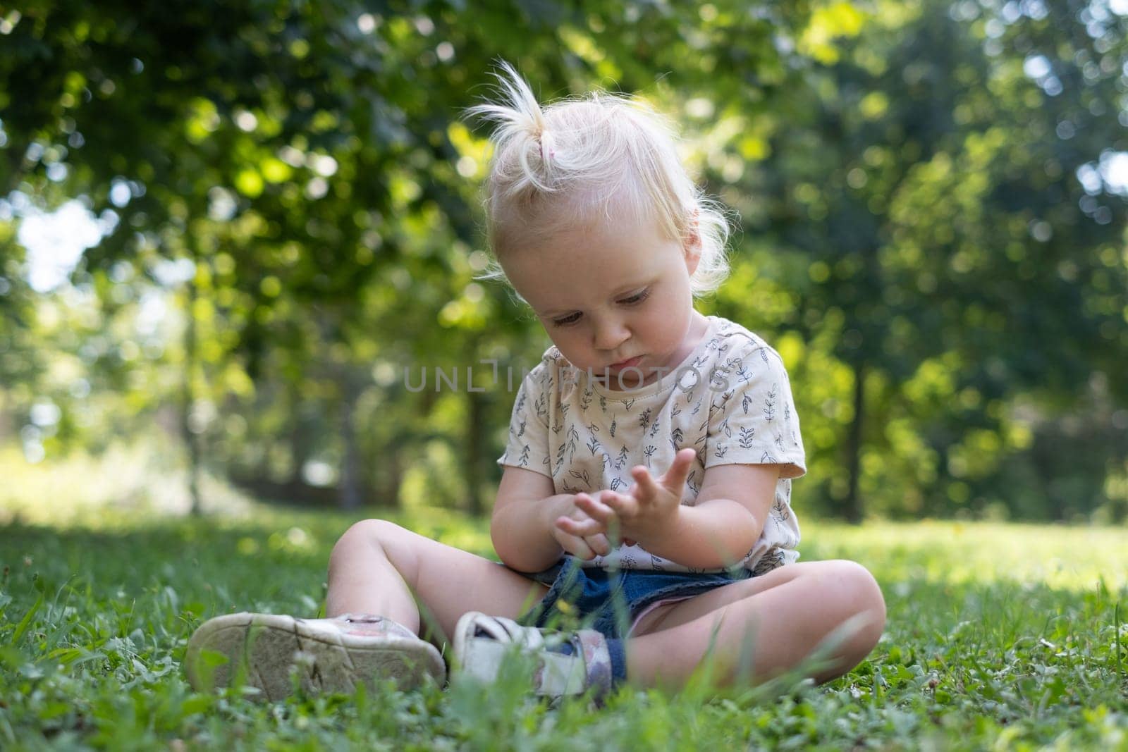 Funny baby kid outside. Cute adorable baby girl in yellow dress sitting on grass in park outdoors.