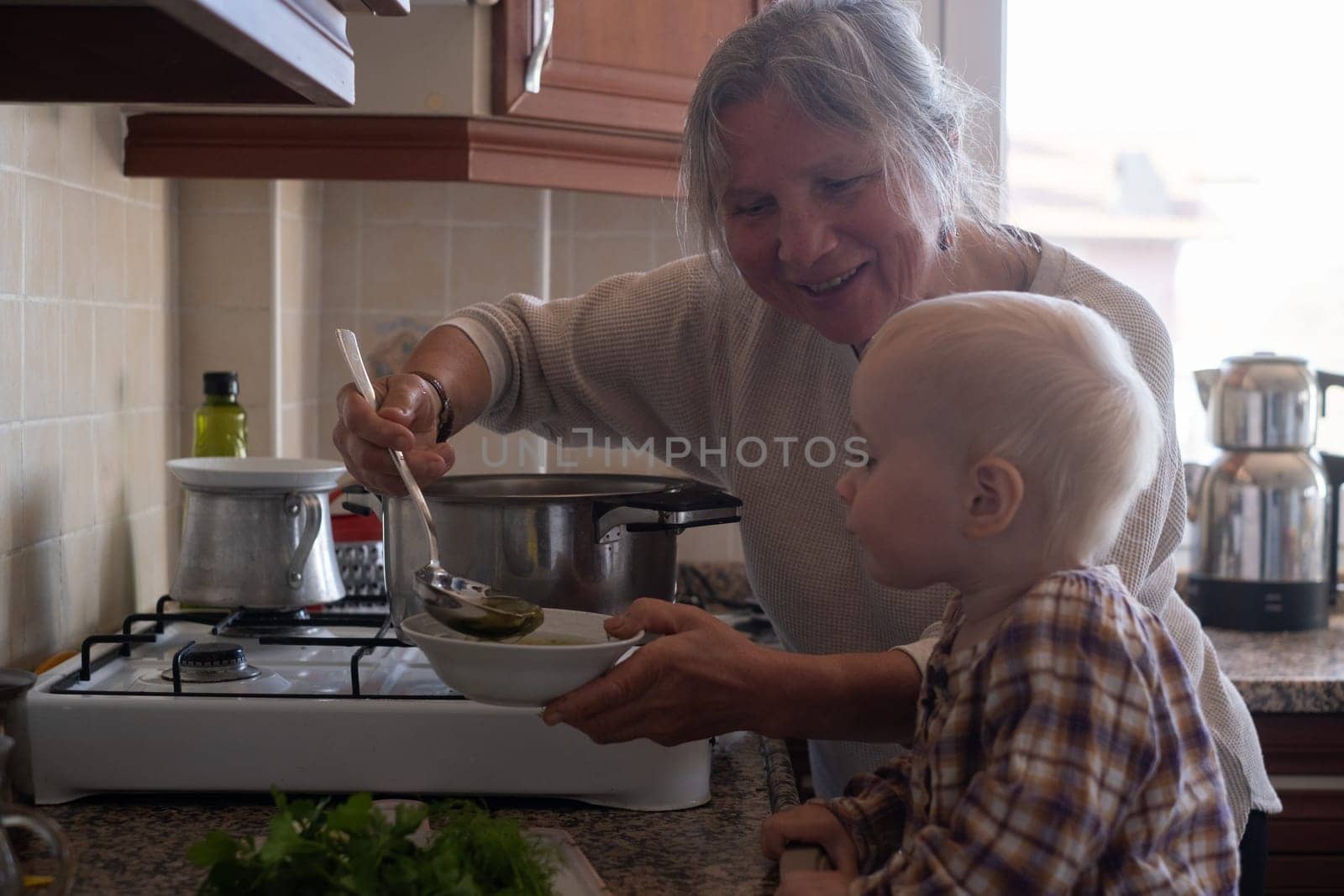 Senior old eldery aged woman grandmother for a toddler cooking soup in kitchen at home. Grandma preparing food, meal. Healthy food, vegetarian concept. Dieting and healthy lifestyle.