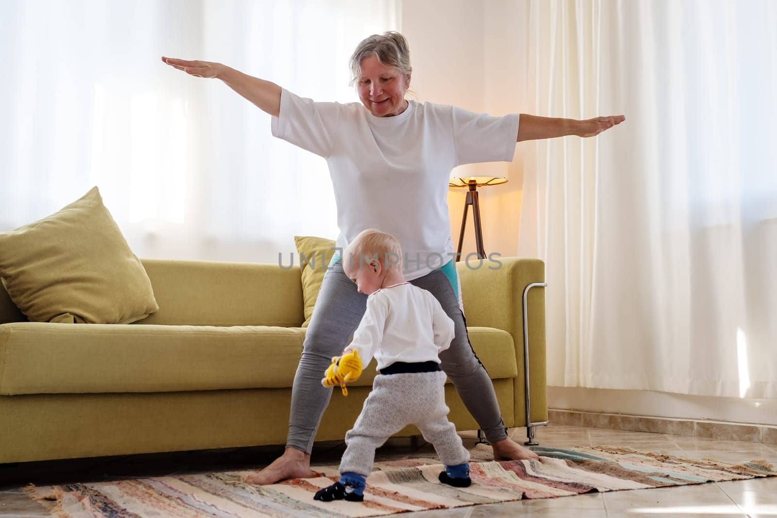 Senior caucasian woman doing yoga at home using chair as a props.