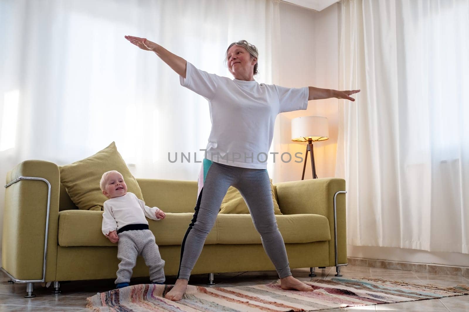 Senior caucasian woman doing yoga at home using chair as a props.