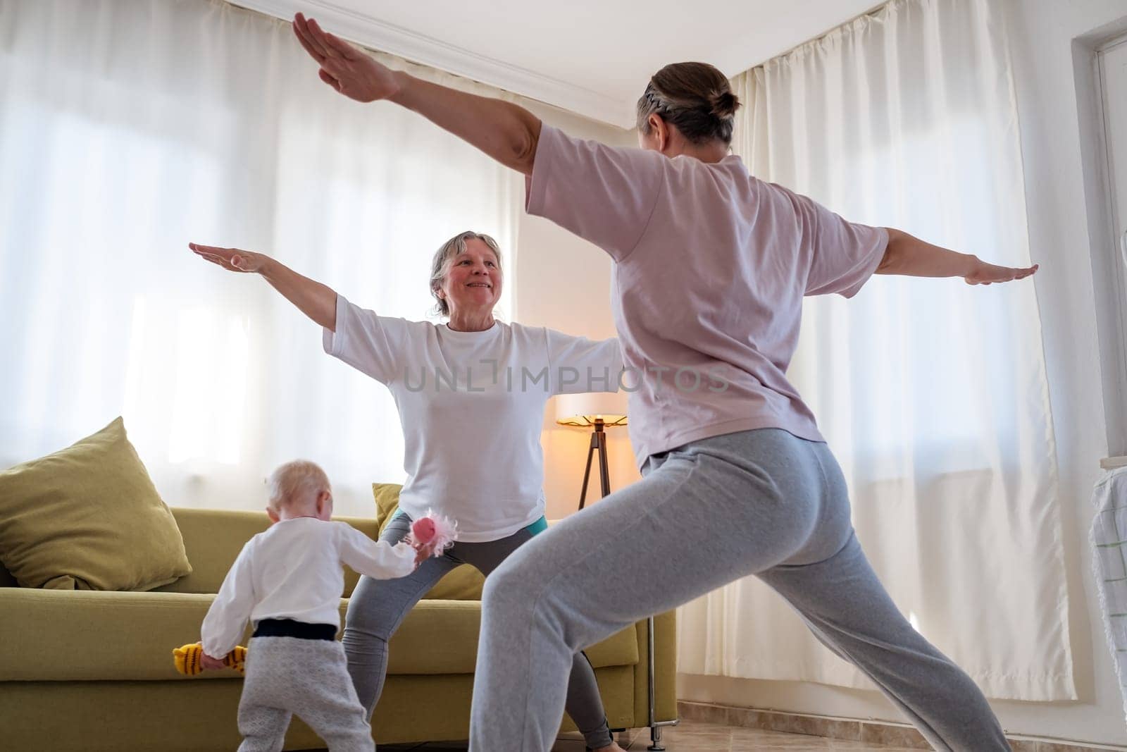 Senior woman exercising at home together with daughter. Active mature woman doing stretching exercise in living room at home.