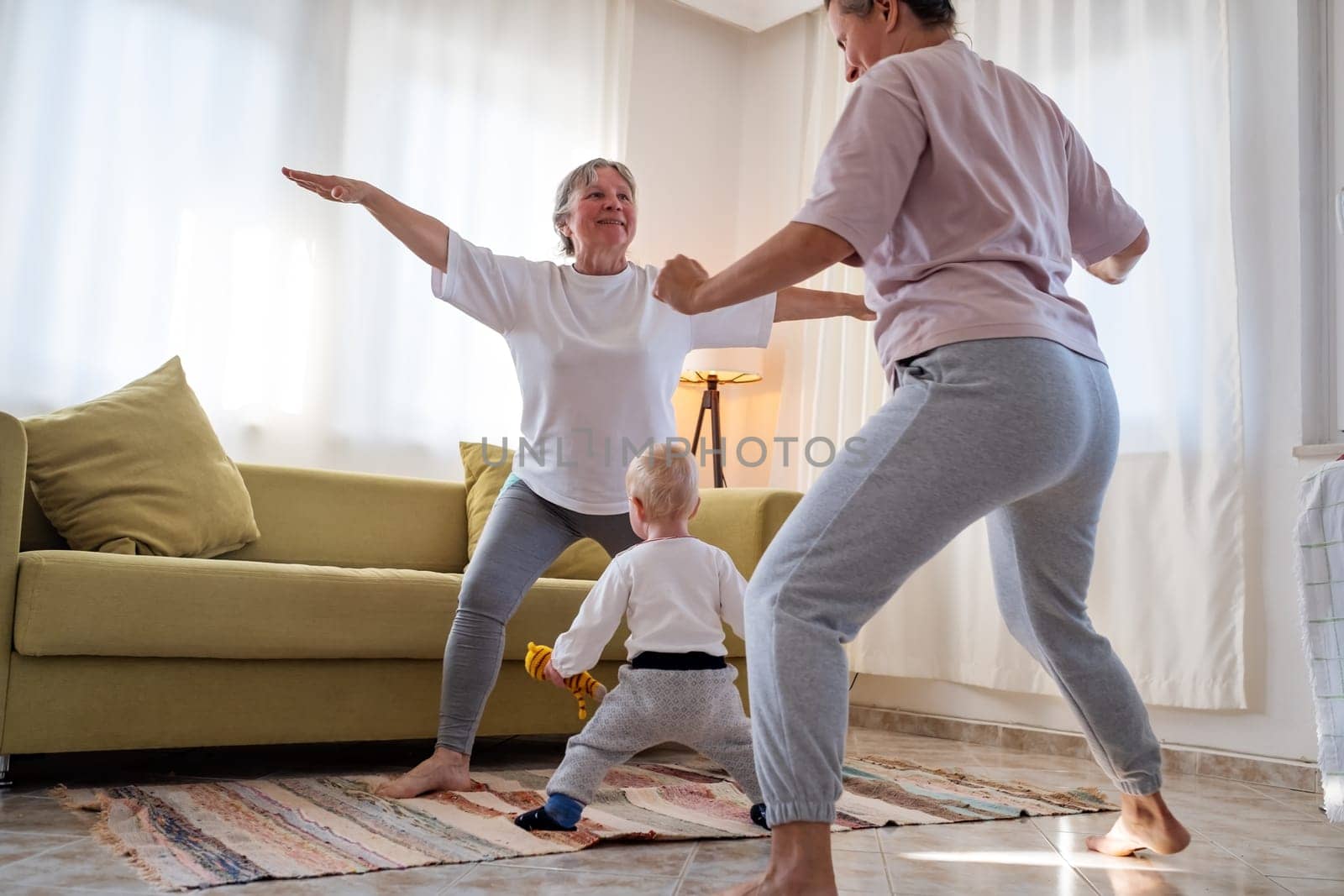 Senior woman exercising at home together with daughter. Active mature woman doing stretching exercise in living room at home.