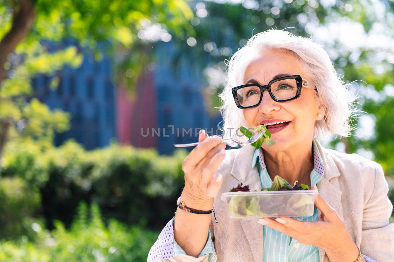 portrait of a middle age woman eating a takeaway salad sitting outdoors in a city park, concept of healthy food and active lifestyle in adulthood, copyspace for text