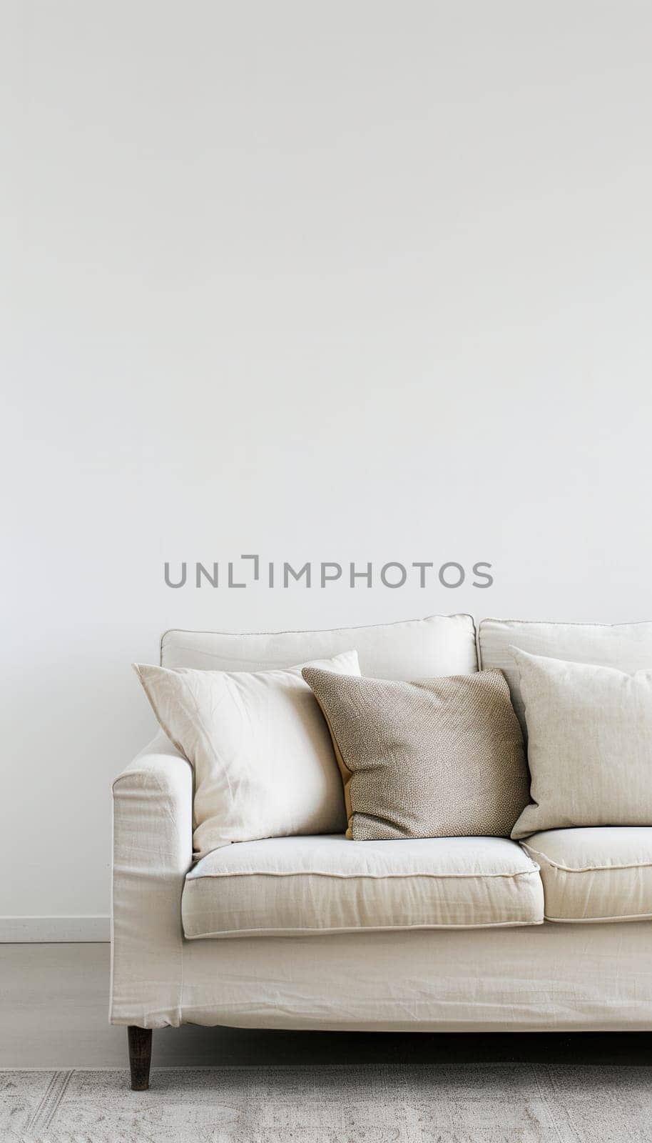 A white couch with three cushions sits in front of a white wall. The couch is on a light-colored rug.