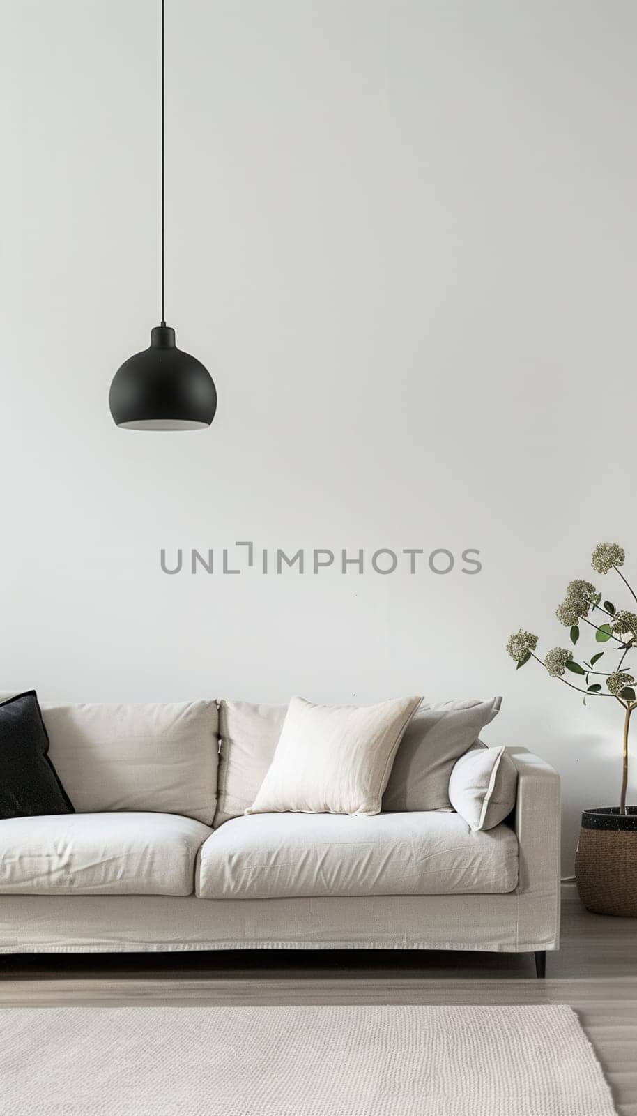A white sofa with plush pillows sits in a bright, minimalist interior, illuminated by a black pendant light hanging from the ceiling.