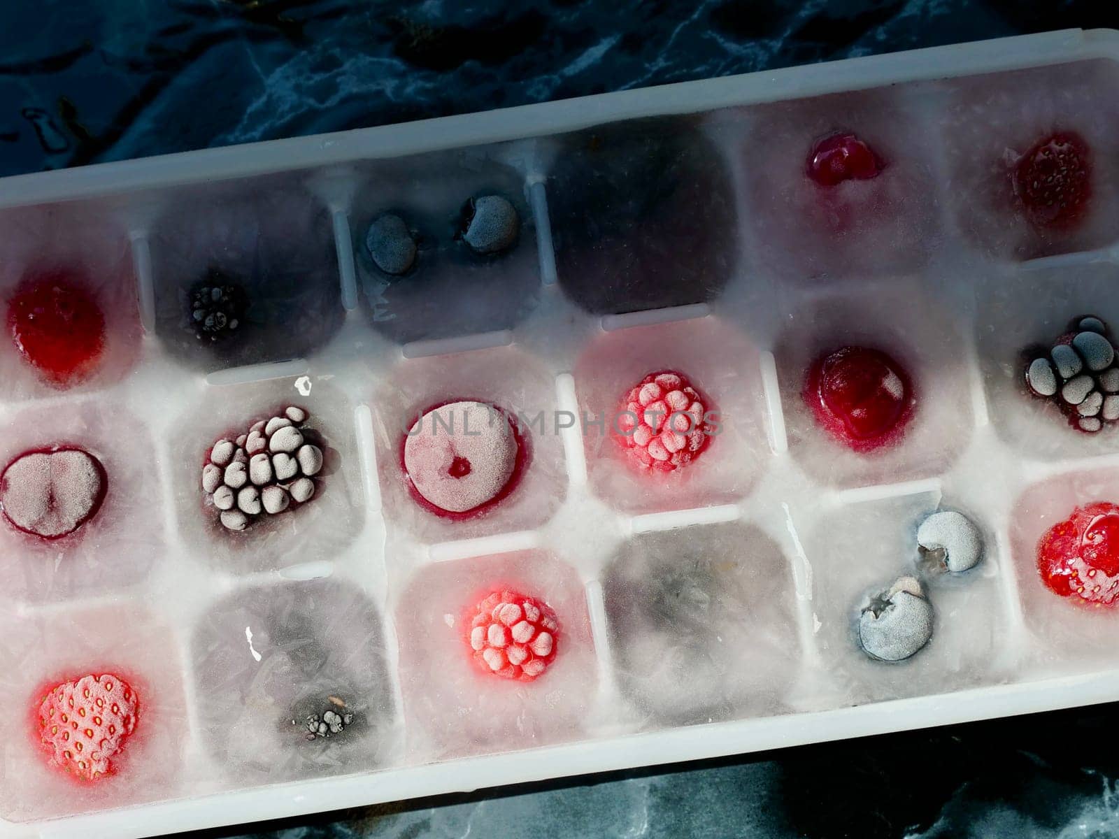 Frozen ice with berries in a container by the piece for making refreshing drinks or preserving vitamins and minerals seasonal cherries, raspberries, strawberries, blackberries, mulberries, blueberries