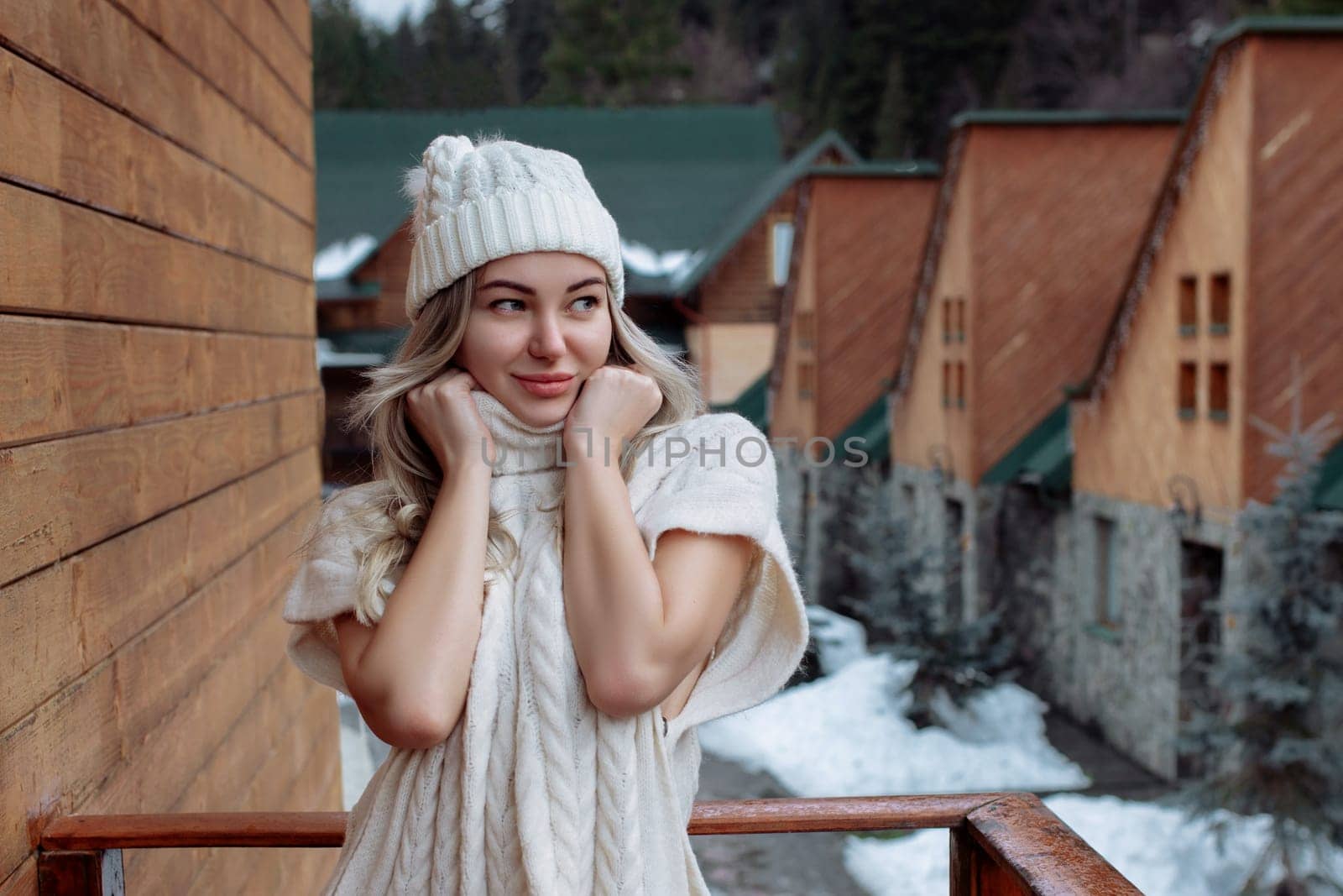 Portrait of a beautiful girl in a white hat and sweater on the street on the balcony. Warm winter clothes.