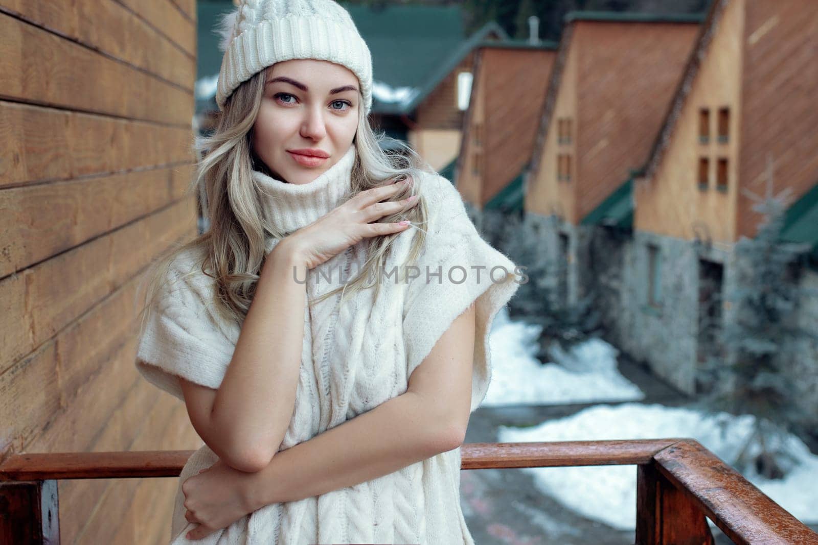 Portrait of a beautiful girl in a white hat and sweater on the street on the balcony. Warm winter clothes.